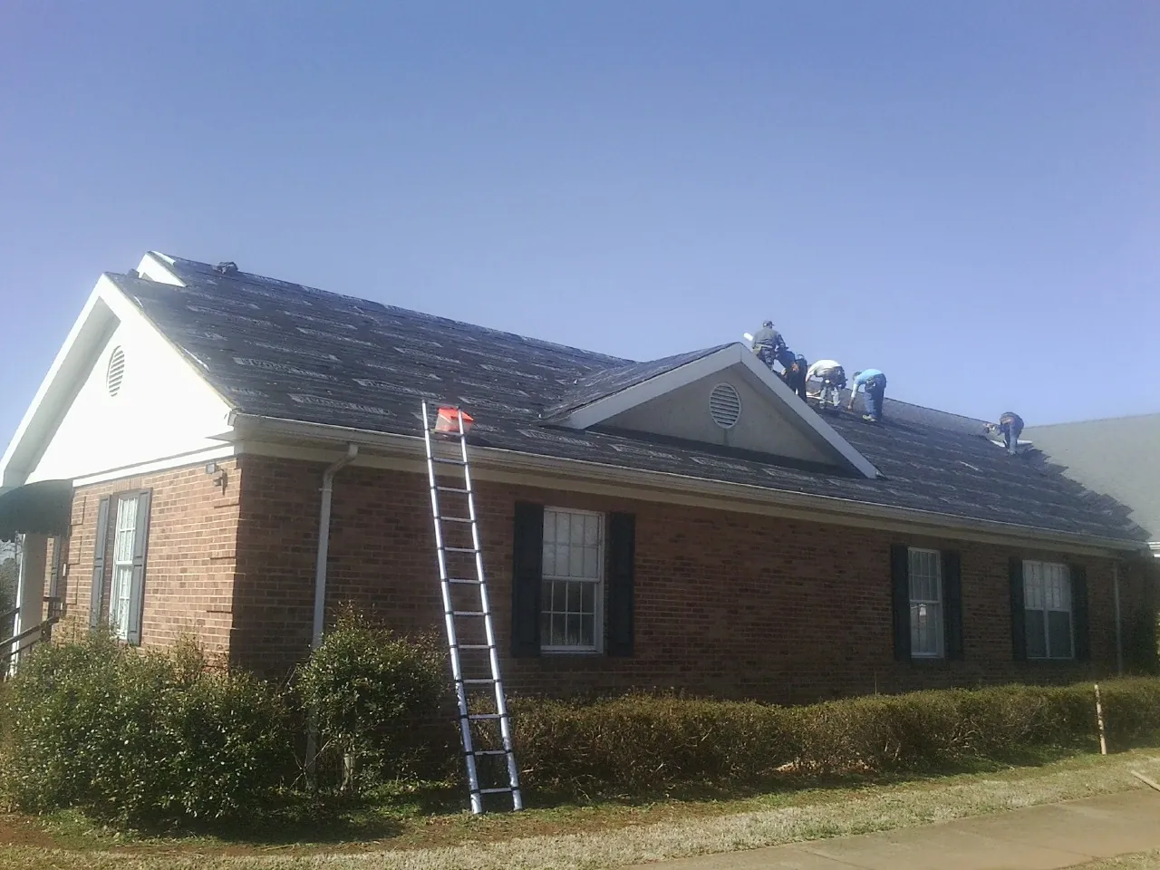 Crew tearing shingles off a brick ranch roof with a ladder set — Emergency Roof Repair work by our crew in Robertsville