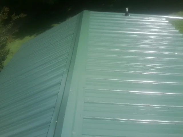 New green metal panels meeting at the ridge of a roof — Flat Roof Repair work by our crew in Robertsville