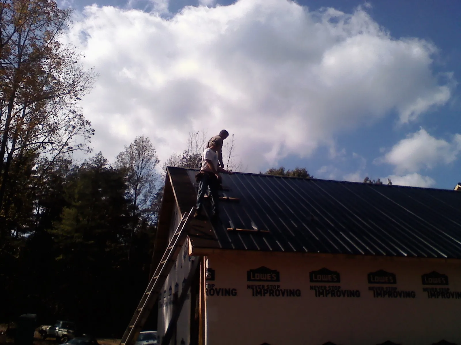 Roofer fastening dark metal panels high against a cloudy sky, from a Roof Inspection job in Robertsville