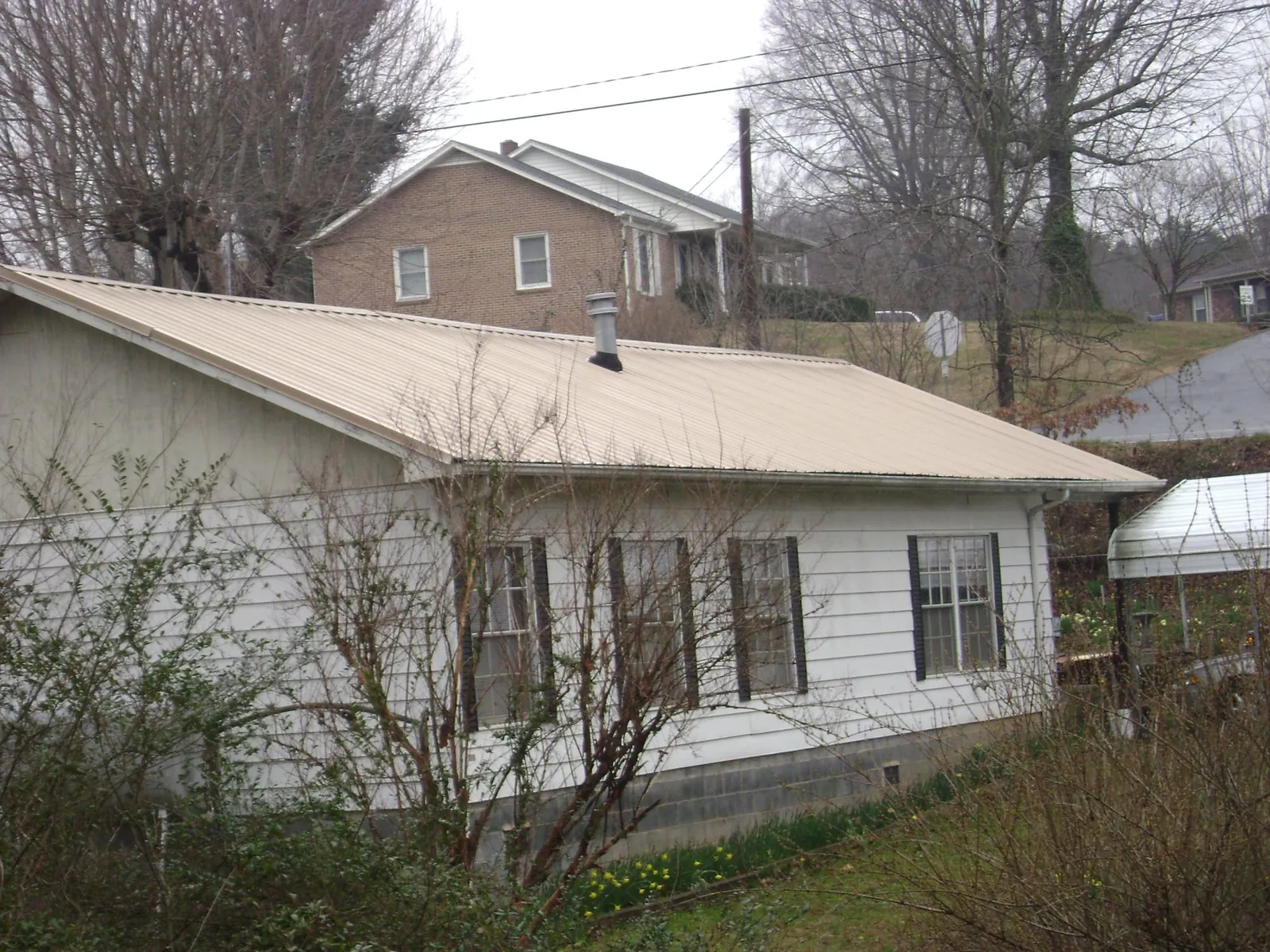 Tan metal roof on a white sided house set into a hillside — Commercial Roofing by Roofing Brothers in Robertsville